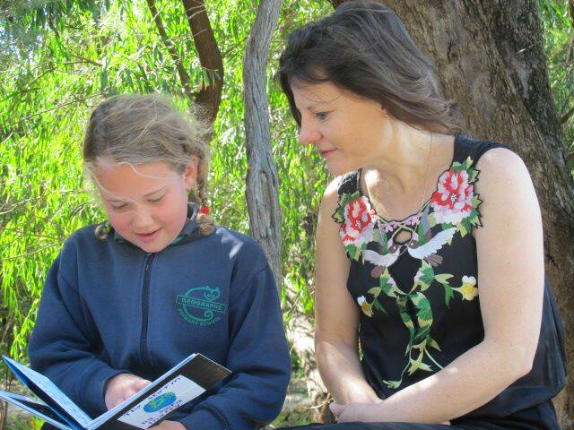Student Sara Ingrey with finalist Ana Nail reading an illustrated story in the outdoor classroom. 