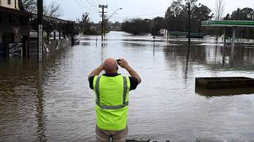 A local takes a photo of a road inundated by floodwaters in Camden in South Western Sydney. Photo: AAP Image/Mick Tsikas