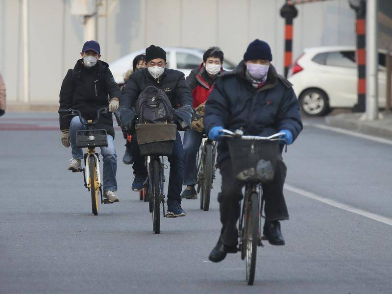 Mask-wearing people ride bicycles on a street in Beijing.