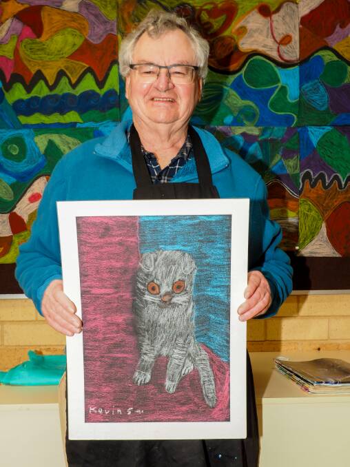 Kevin Sambell holding his drawing, standing in front of a mosaic created by the Busso Bunch art group.
