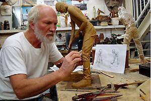Sculptor Greg James adding detail to the clothing of a timber worker figurine.